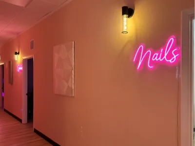 The hallway to the treatment rooms with a pink neon Nails sign
